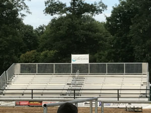 Empty outdoor stadium bleachers with a banner at the top, surrounded by trees .