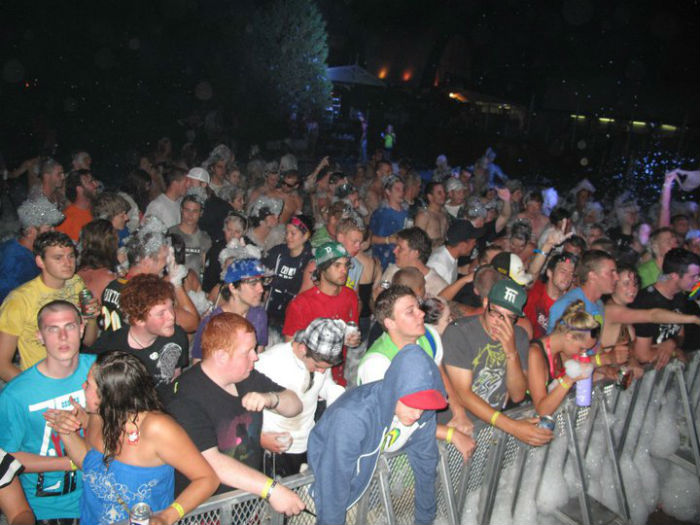 Large nighttime concert crowd pressed against a metal barrier, fans cheering and dancing under dark skies at a show. (Front row scene)