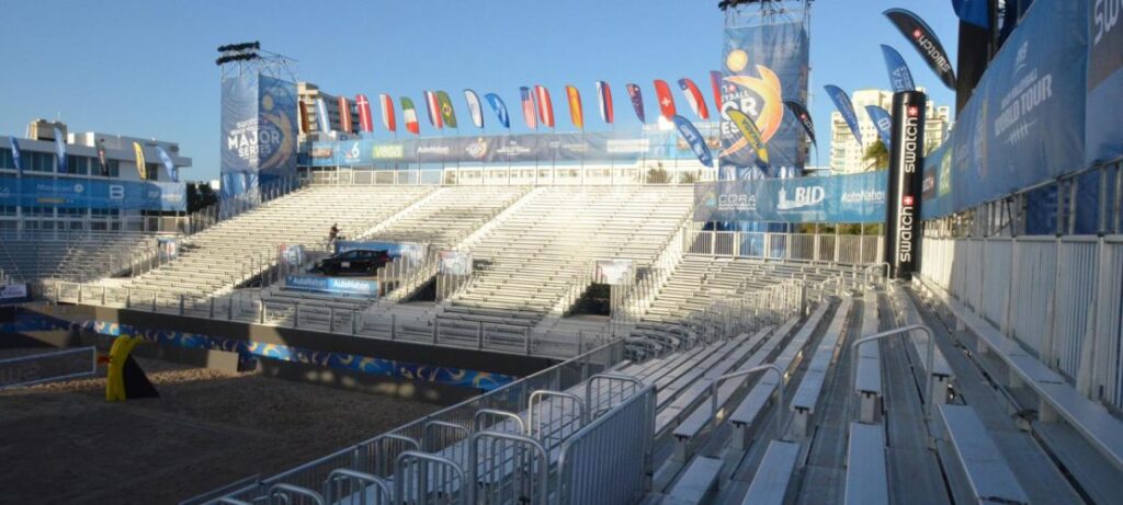 Empty outdoor stadium bleachers with colorful pennant flags and sponsor banners above the seating area.
